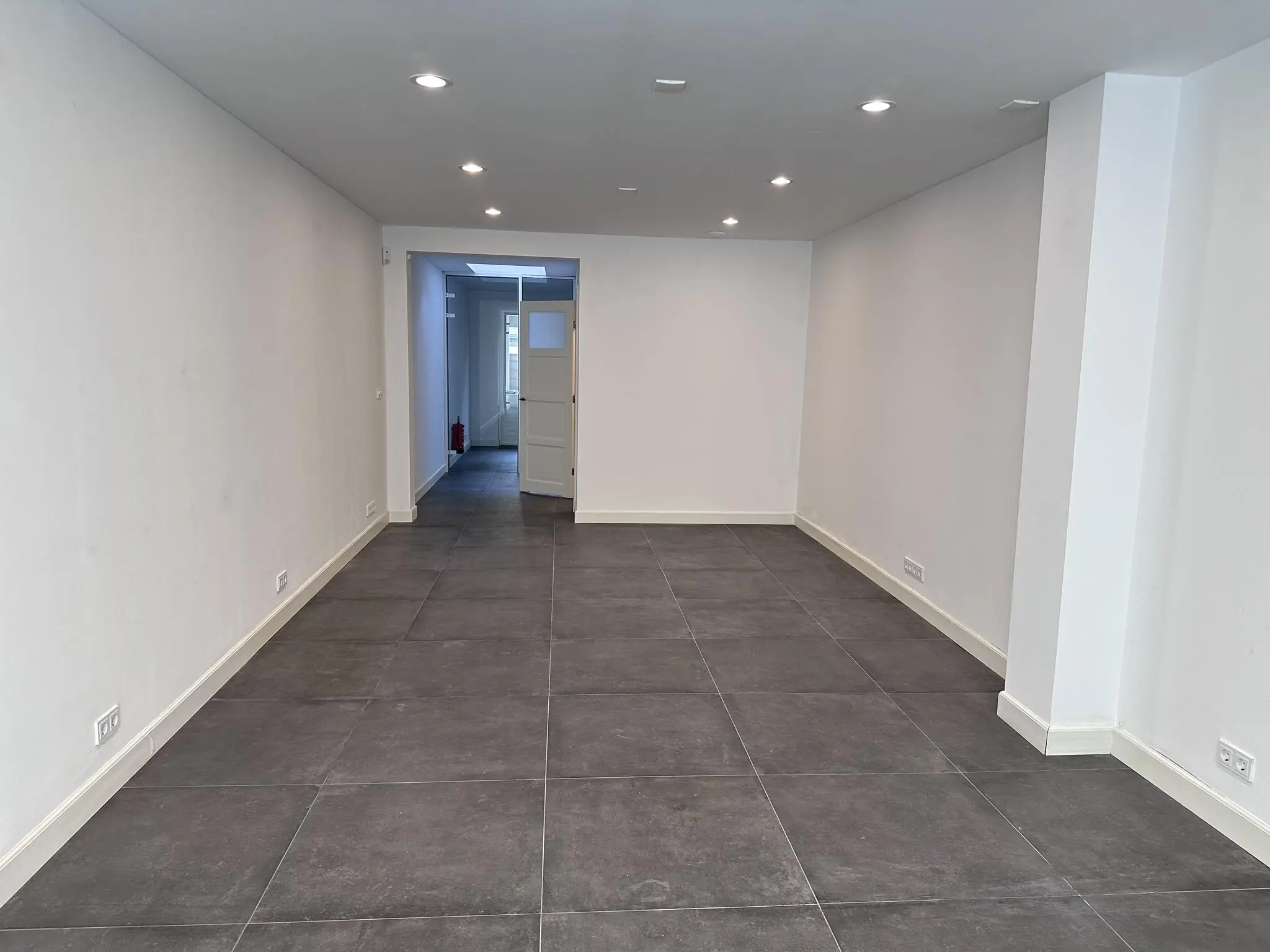 Leeg, smal winkel- of kantoorpand aan de Ceintuurbaan met grijze vloertegels en witte muren.
