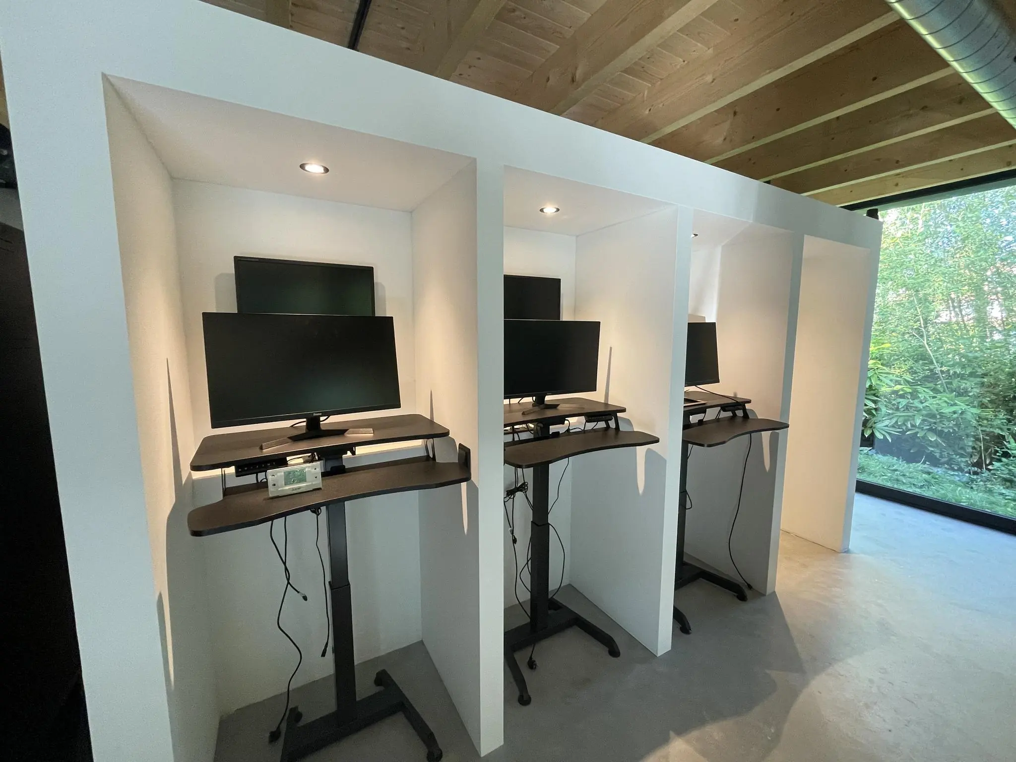 Moderne werkplekken met zit-sta bureaus en dubbele monitoren in afgesloten cabines aan de Sloterweg.