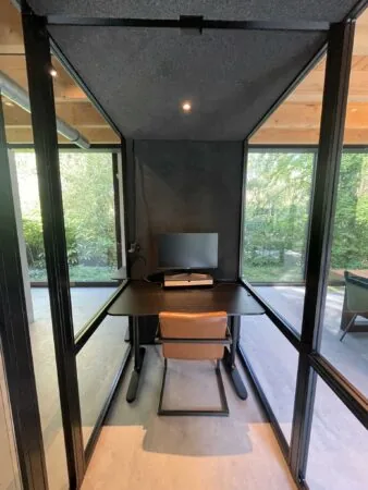 Kleine glazen werkruimte met een bureau, stoel en computerscherm aan de Sloterweg omgeven door groen.