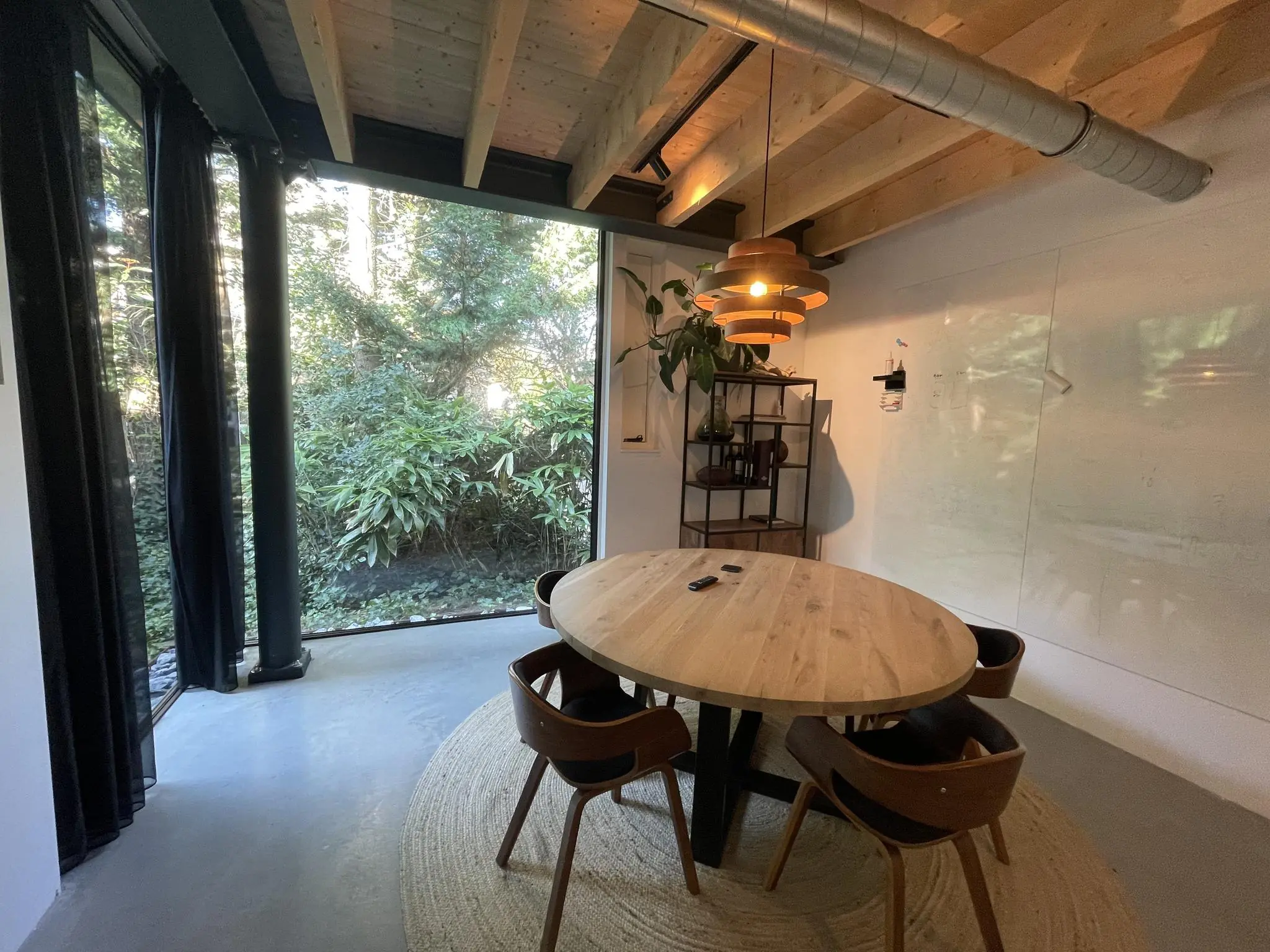 Moderne vergaderruimte aan de Sloterweg met houten tafel, designstoelen, groot raam met uitzicht op groen en een whiteboardwand.