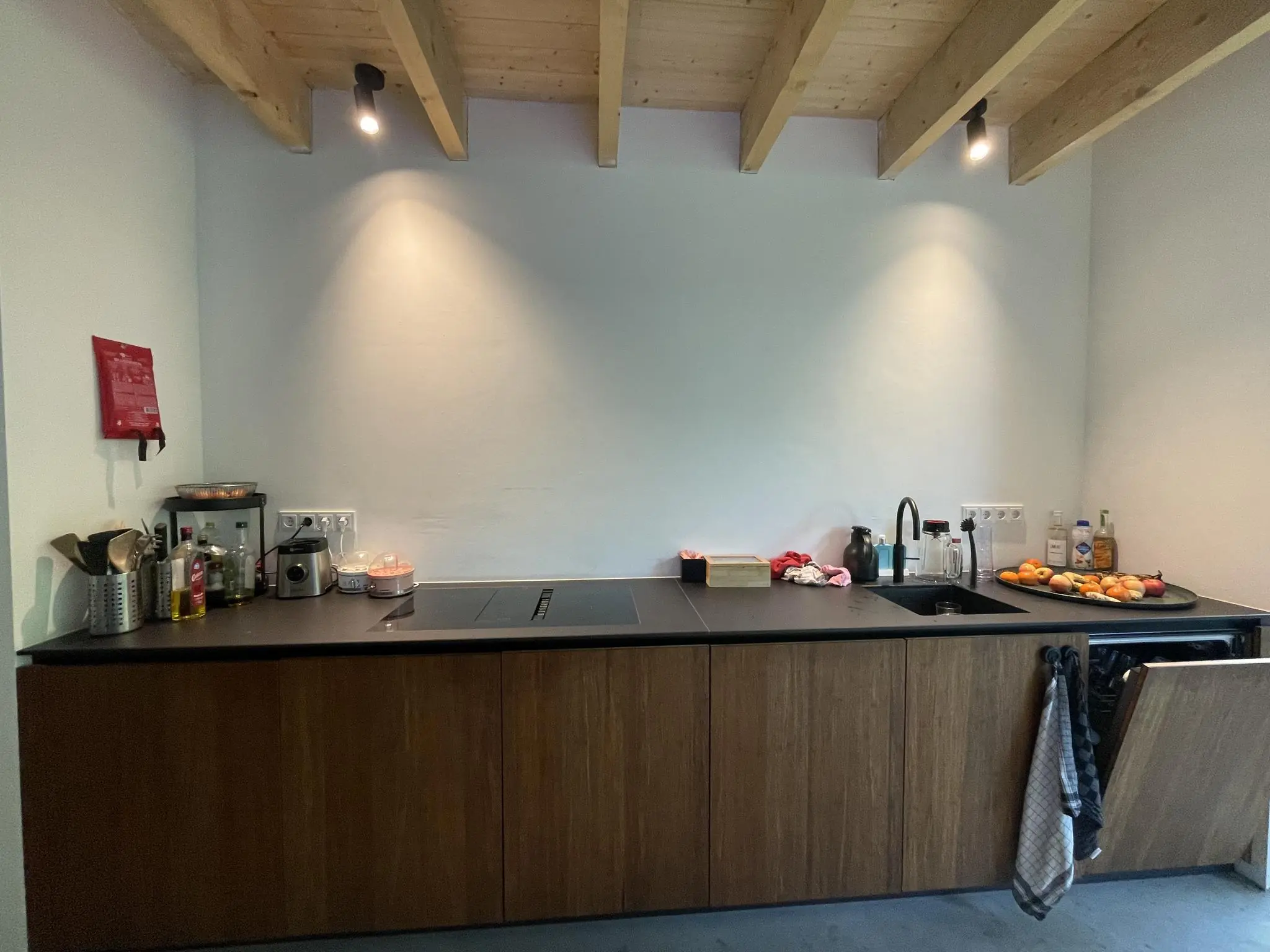 Moderne keuken aan de Sloterweg met houten kastjes, zwarte werkblad en diverse keukenspullen op het aanrecht.