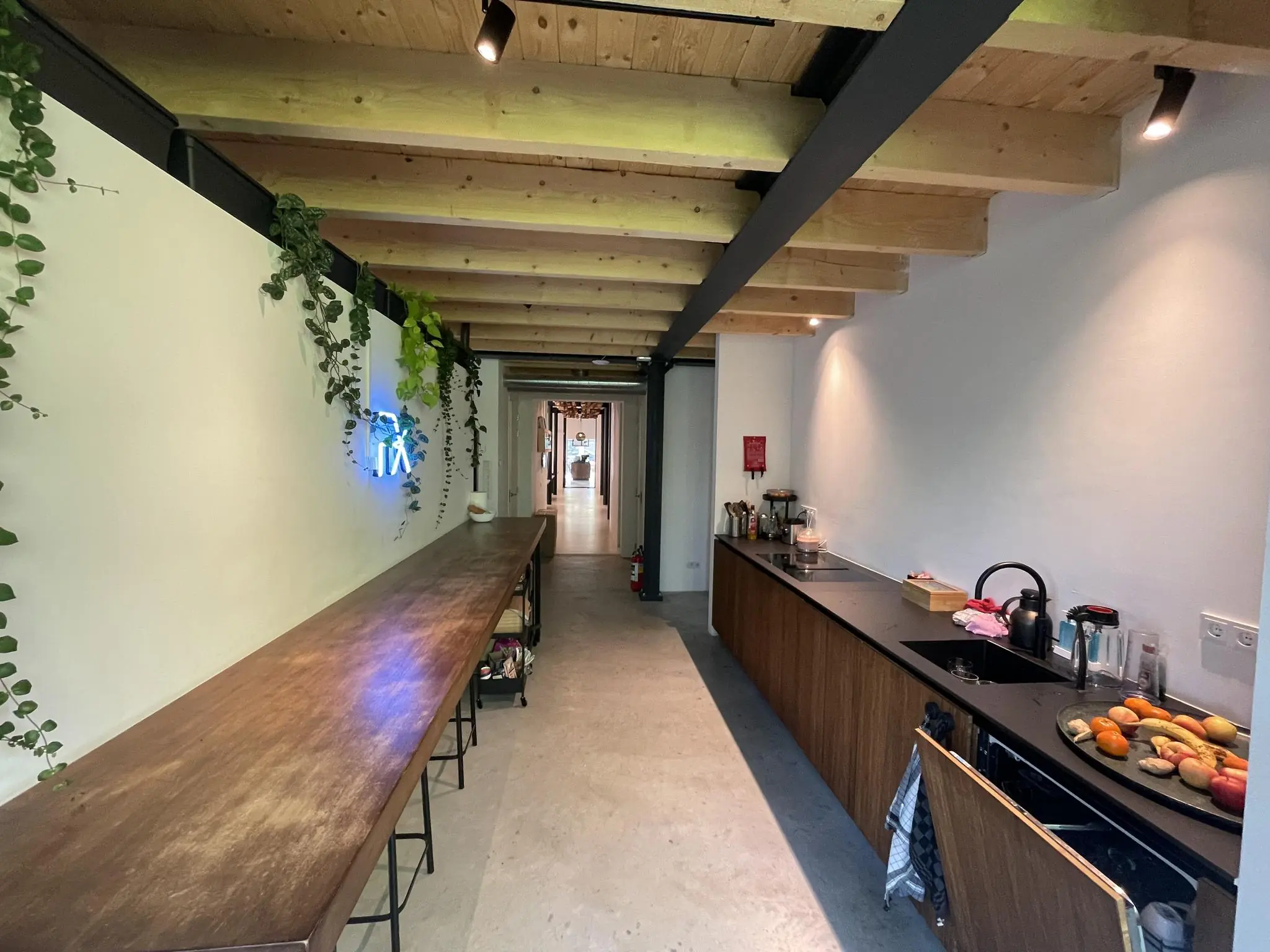 Moderne keuken aan de Sloterweg met houten balkenplafond, lange houten tafel, planten en een minimalistisch keukenblok.