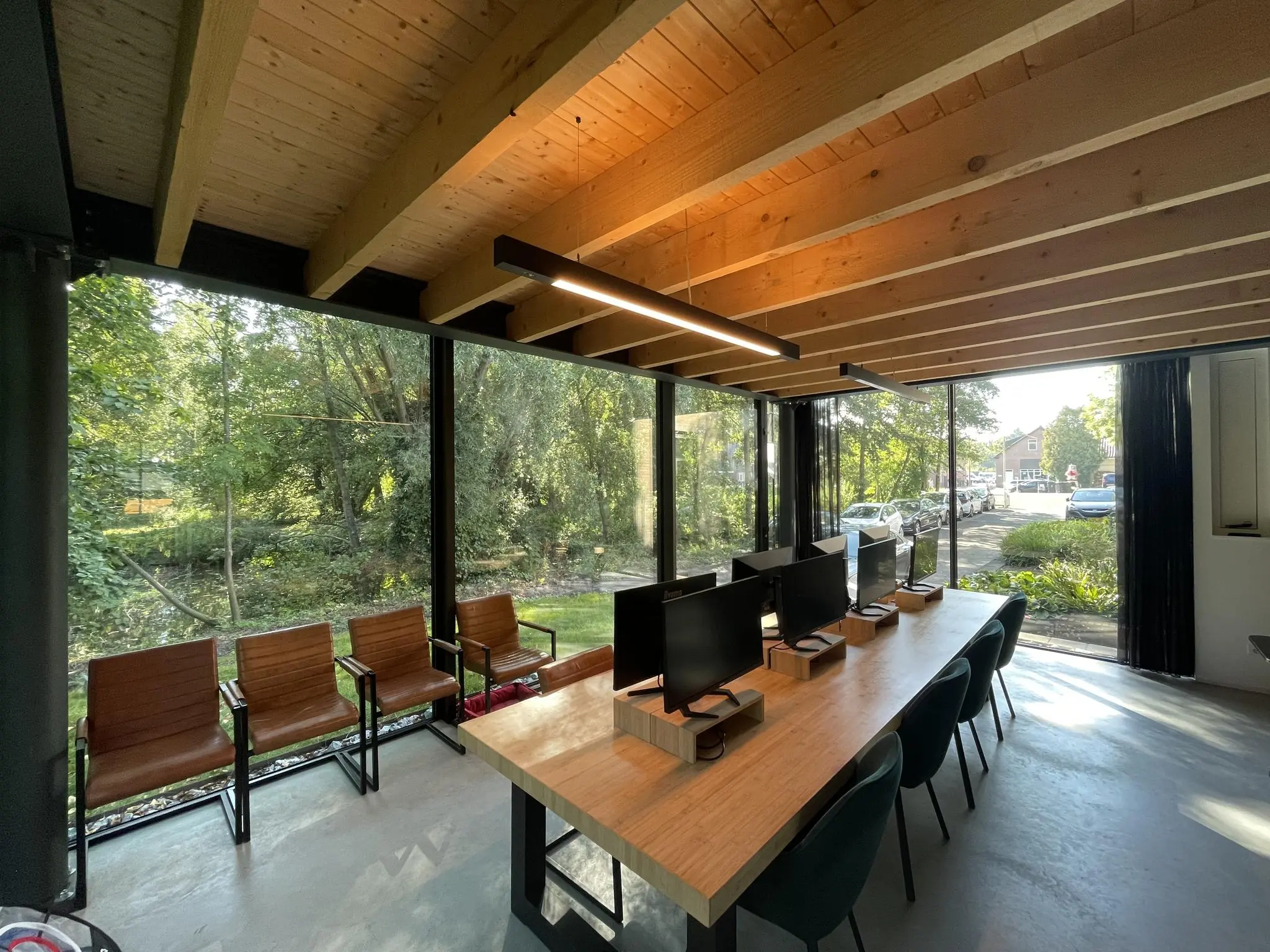 Moderne kantoorruimte aan de Sloterweg met houten plafond, werkplekken en grote ramen met uitzicht op groen en een straat.