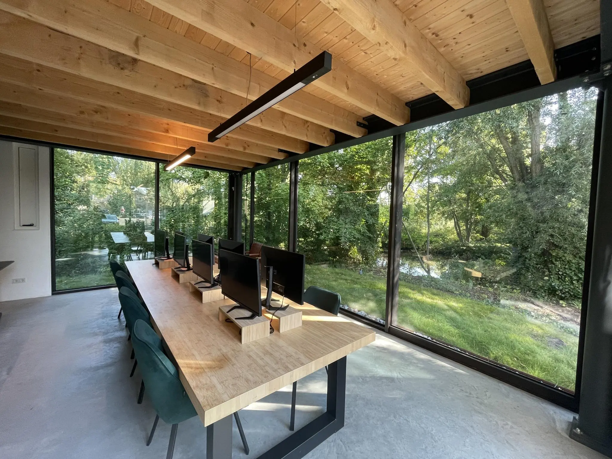 Moderne kantoorruimte aan de Sloterweg met houten plafond, grote ramen en uitzicht op een groene, bosrijke omgeving.