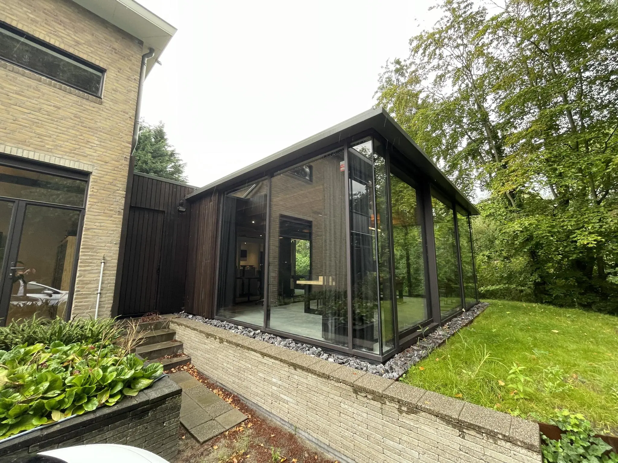 Moderne uitbouw met glazen wanden aan een woning aan de Sloterweg, grenzend aan een groene tuin.