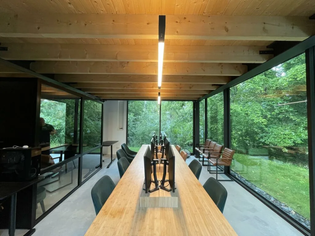 Moderne kantoorruimte aan de Sloterweg met houten plafond, lange werktafel en grote ramen met uitzicht op groen.