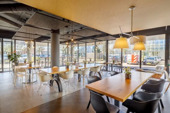 Moderne, sfeervol ingerichte kantoorlounge aan de Hogehilweg met houten tafels, designstoelen en grote ramen met uitzicht op de straat.