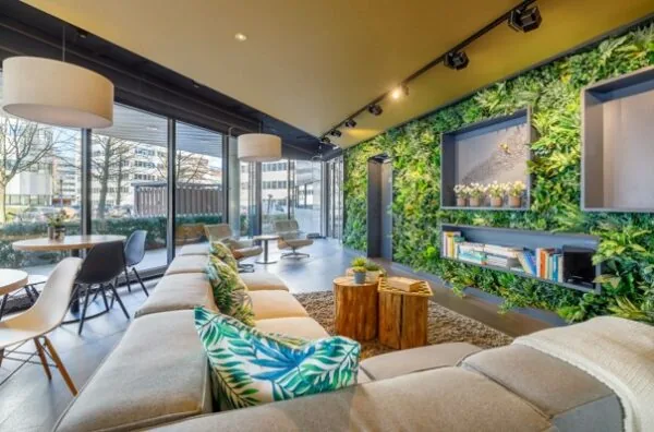 Moderne lounge met grote ramen, groene moswand, comfortabele zitplekken en natuurlijke accenten in een kantoor aan de Hogehilweg.
