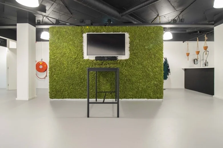 Moderne kantoorruimte aan de Hogehilweg met een groene moswand, flatscreen-tv en minimalistisch interieur.