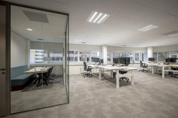 Modern kantoorinterieur aan de Hogehilweg met open werkplekken en een vergaderruimte met glazen wand.
