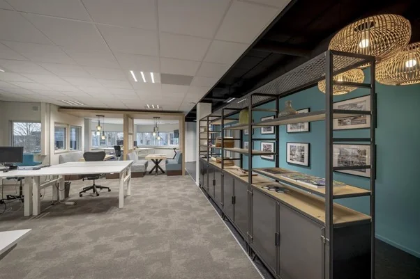 Modern kantoorinterieur aan de Hogehilweg met open werkplekken, wandrekken en decoratieve verlichting.