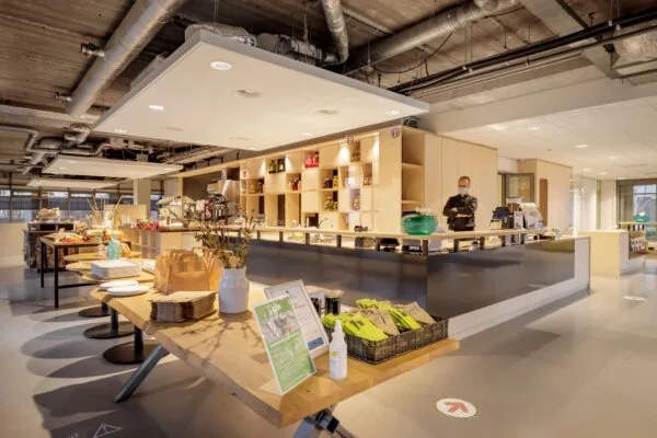 Moderne en sfeervol ingerichte bedrijfskantine aan de Karspeldreef met een open keuken en uitgestalde etenswaren.