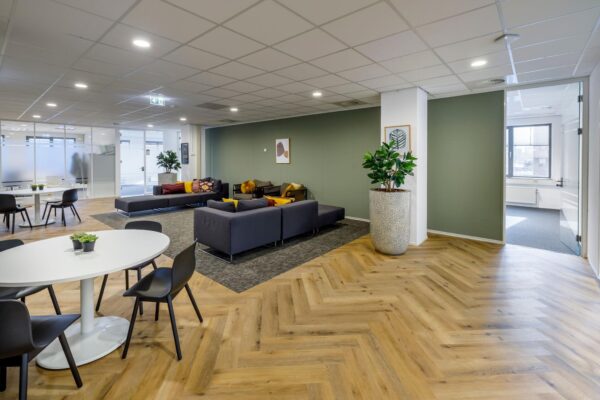 Moderne en open kantoorlounge aan de Karspeldreef met zithoeken, ronde tafels en houten visgraatvloer.