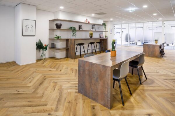 Moderne en open kantoorruimte aan de Karspeldreef met houten visgraatvloer, werktafels en decoratieve planten.