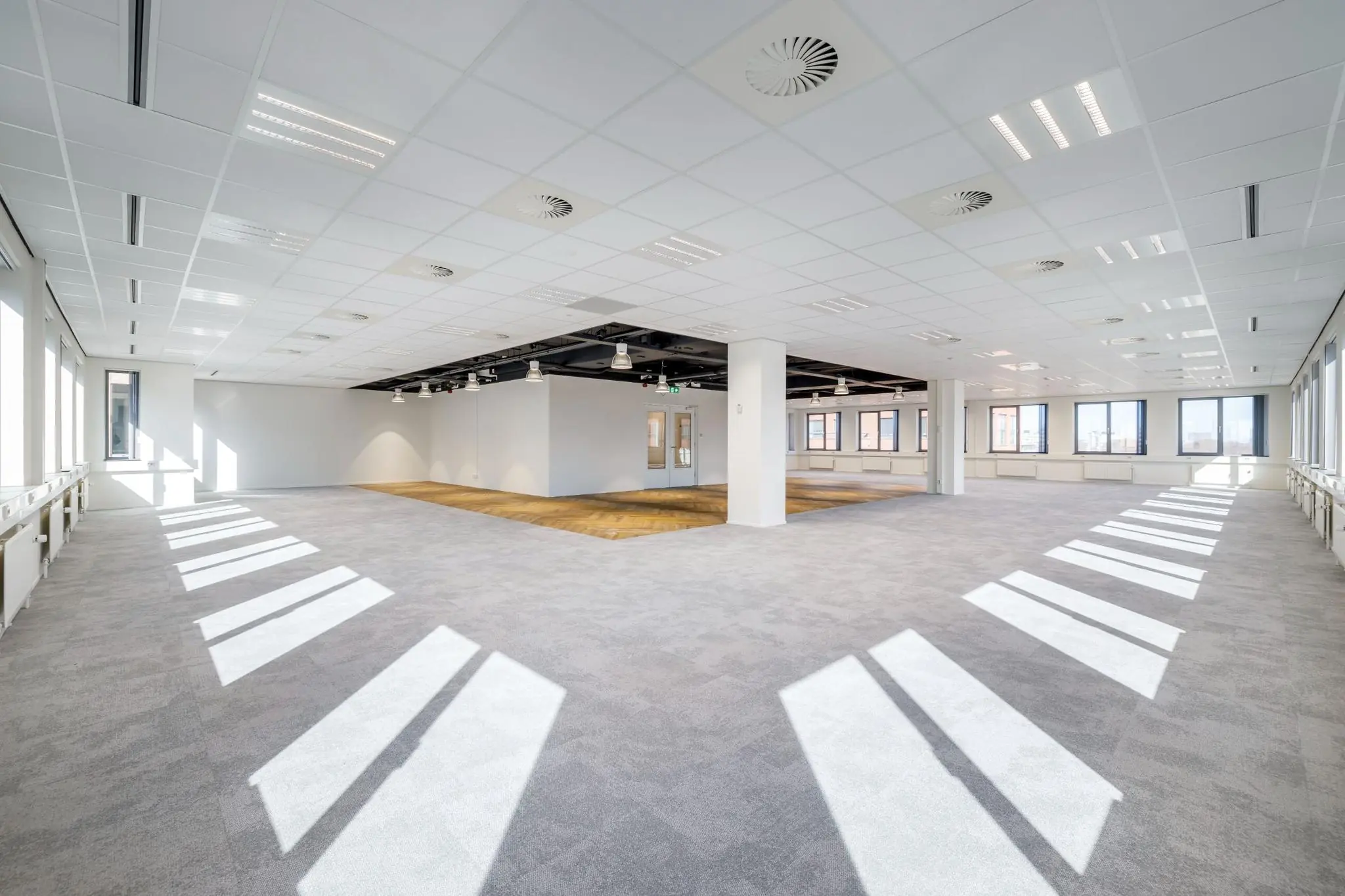 Lichte, ruime kantoorruimte aan de Karspeldreef met grote ramen en een combinatie van tapijt en houten vloer.