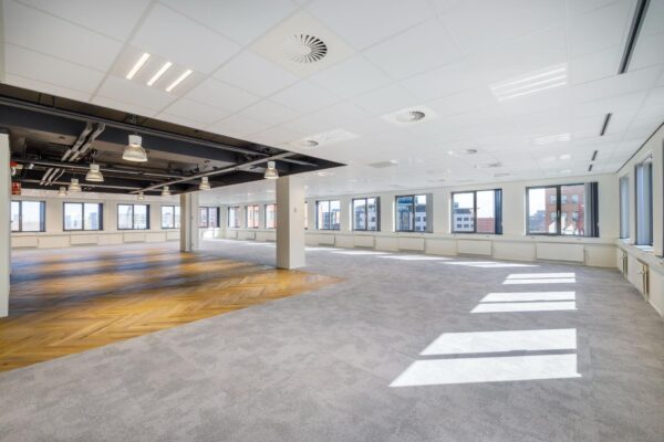 Licht en modern leeg kantoorpand aan de Karspeldreef met grote ramen, systeemplafond en deels houten visgraatvloer.