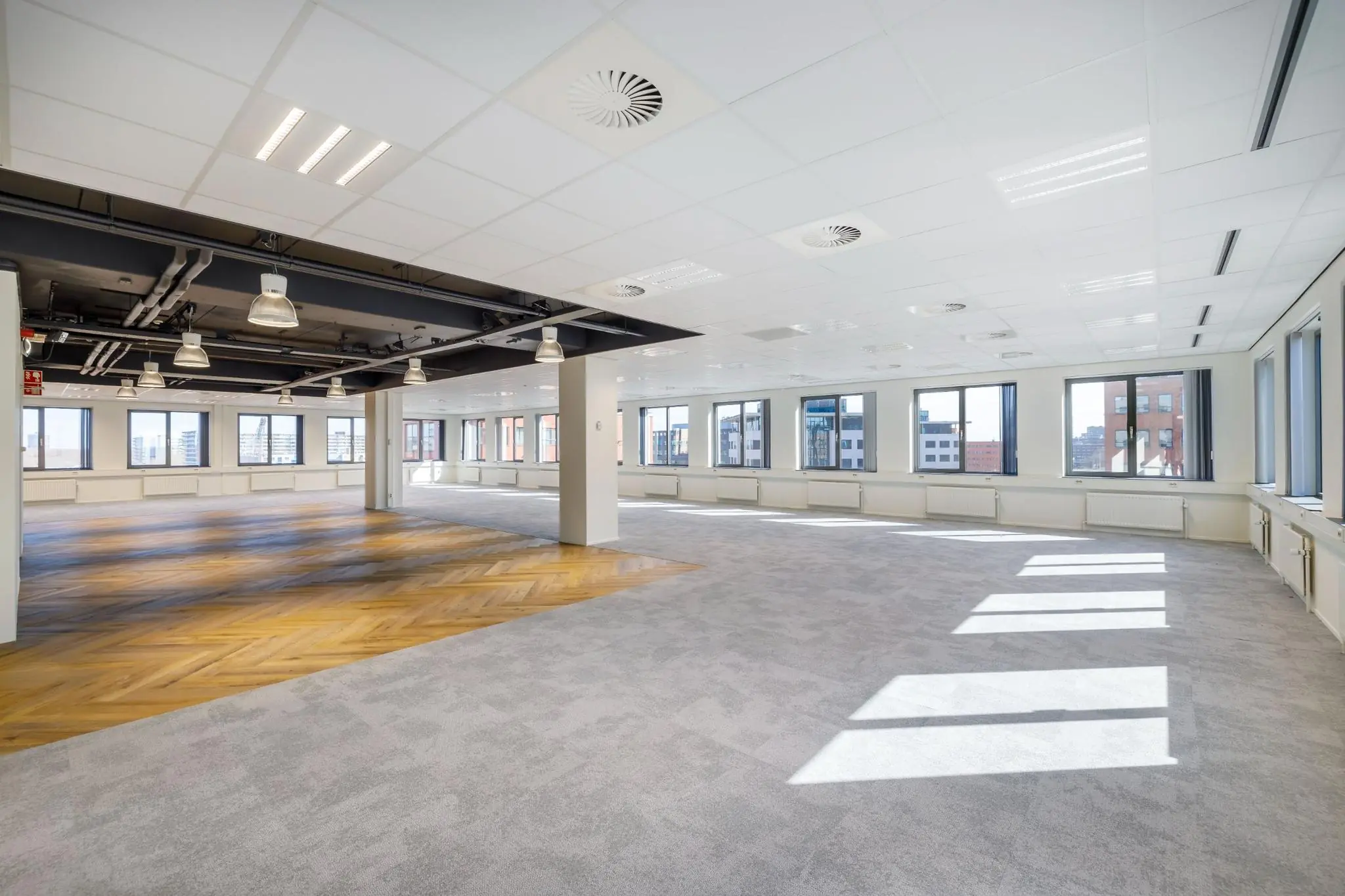 Licht en modern leeg kantoorpand aan de Karspeldreef met grote ramen, systeemplafond en deels houten visgraatvloer.