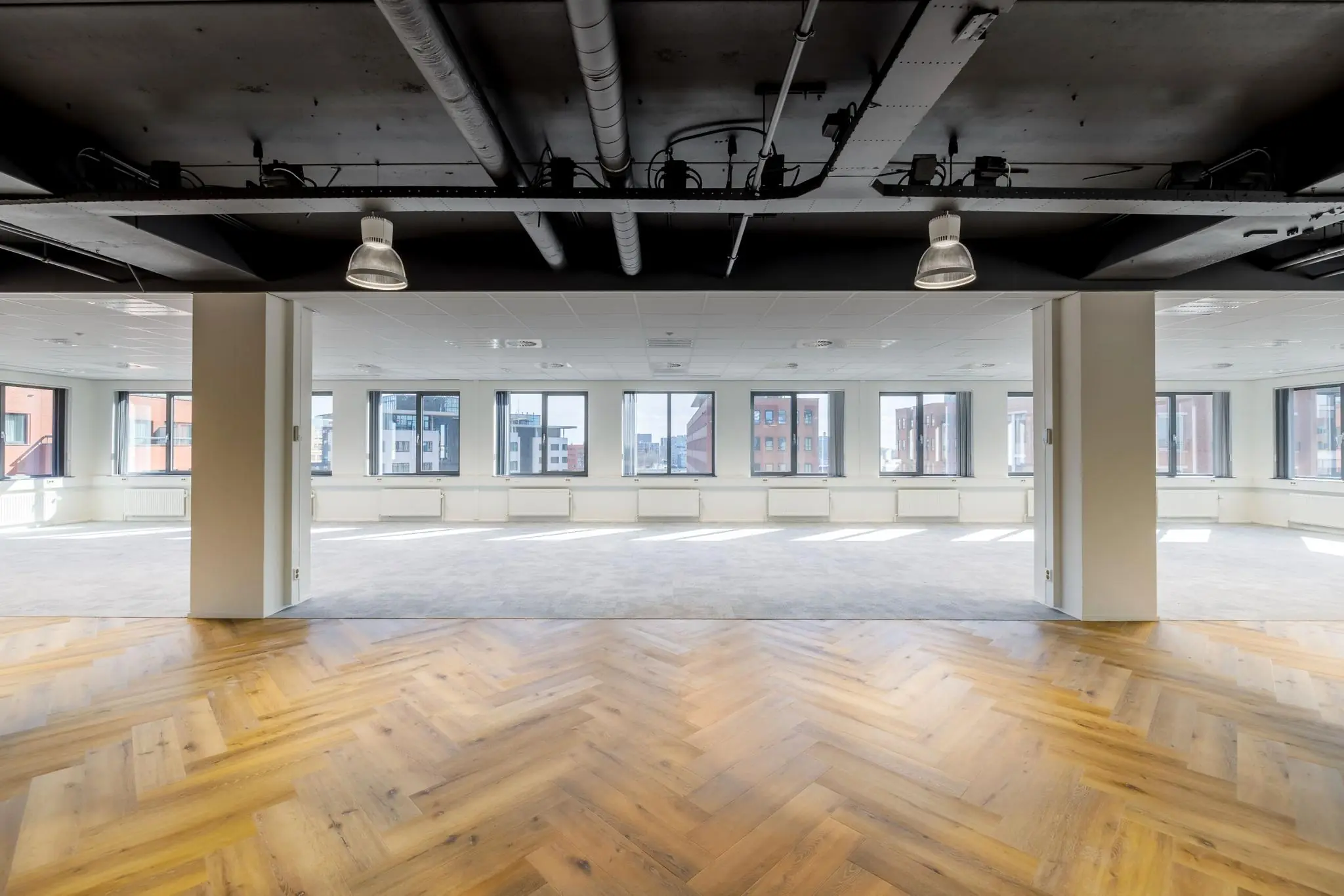 Licht en ruim kantoorinterieur aan de Karspeldreef met visgraat en tapijtvloer, grote ramen en industriële plafonds.