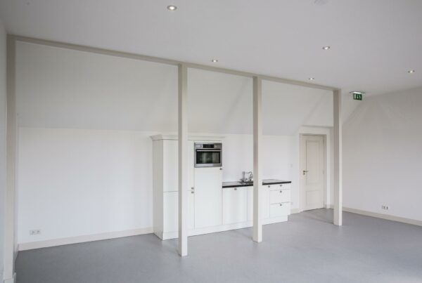 Moderne, witte kitchenette met inbouwapparatuur in een minimalistische ruimte aan de Naarderstraat.