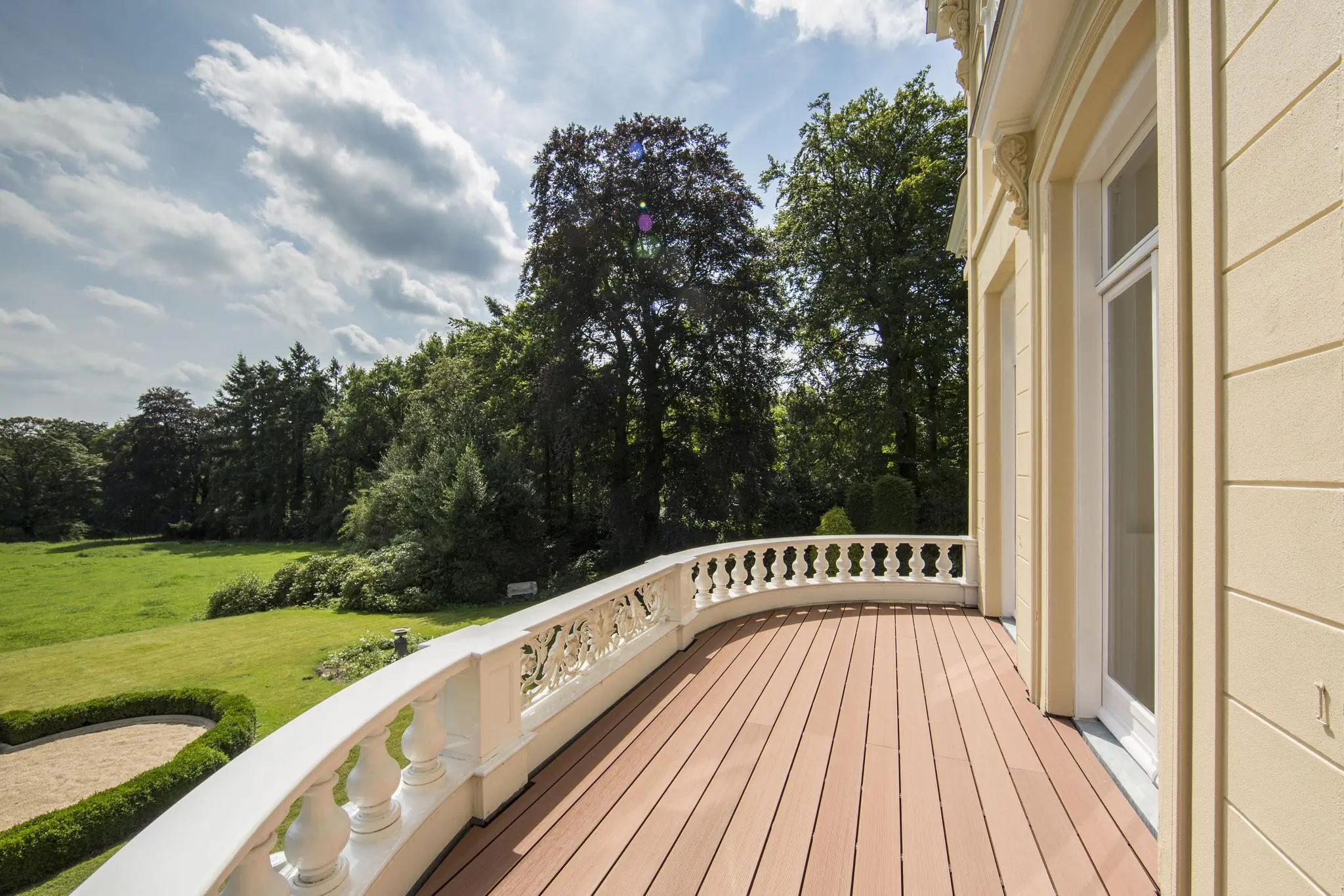 Luxe balkon met houten vloer en witte balustrade, uitkijkend op een groene tuin aan de Naarderstraat.