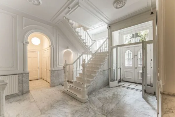 Luxe marmeren entreehal met klassieke trap en dubbele voordeur aan de Naarderstraat.