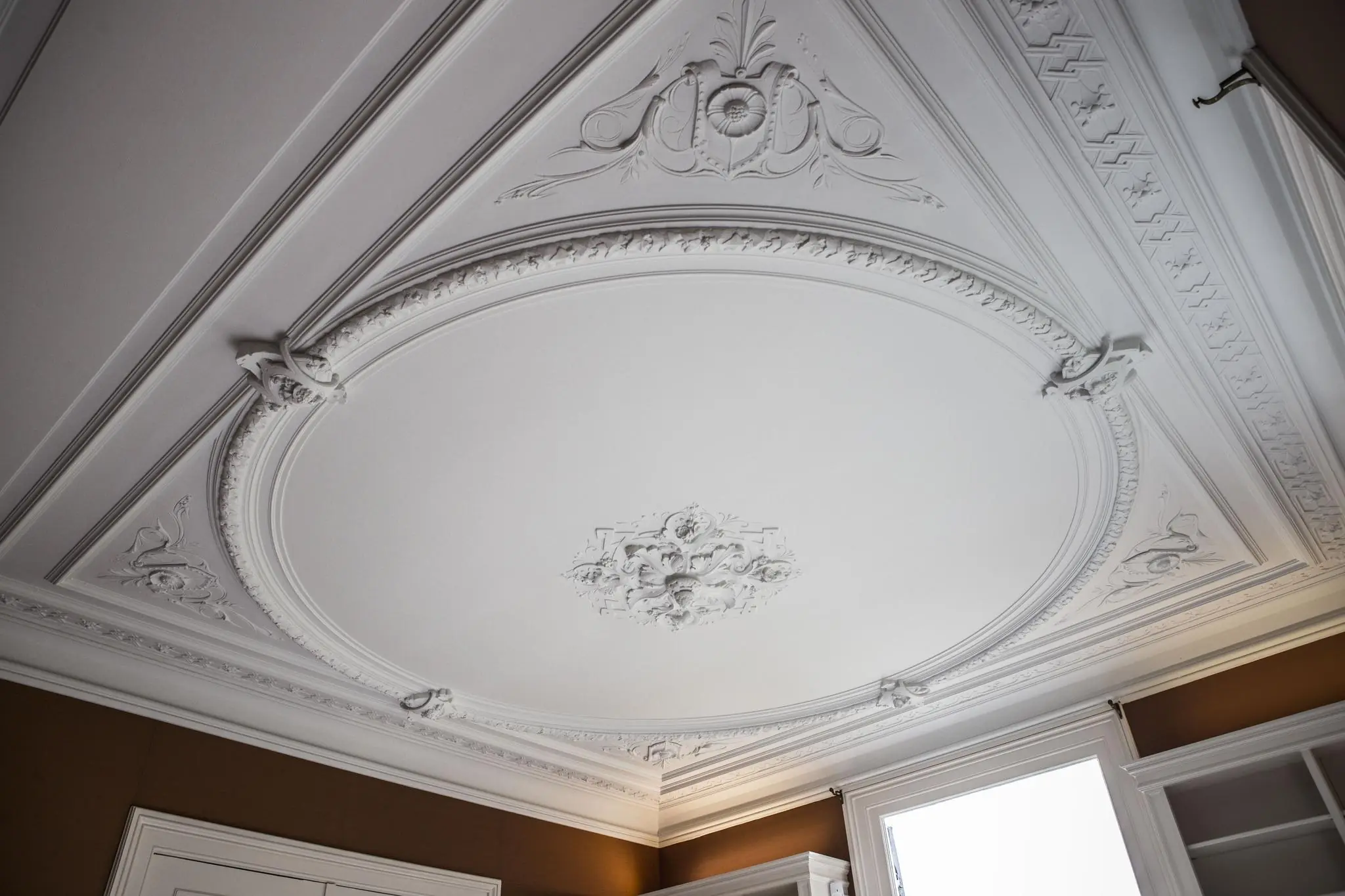 Plafond met sierlijk wit stucwerk en ornamenten in een kamer aan de Naarderstraat.