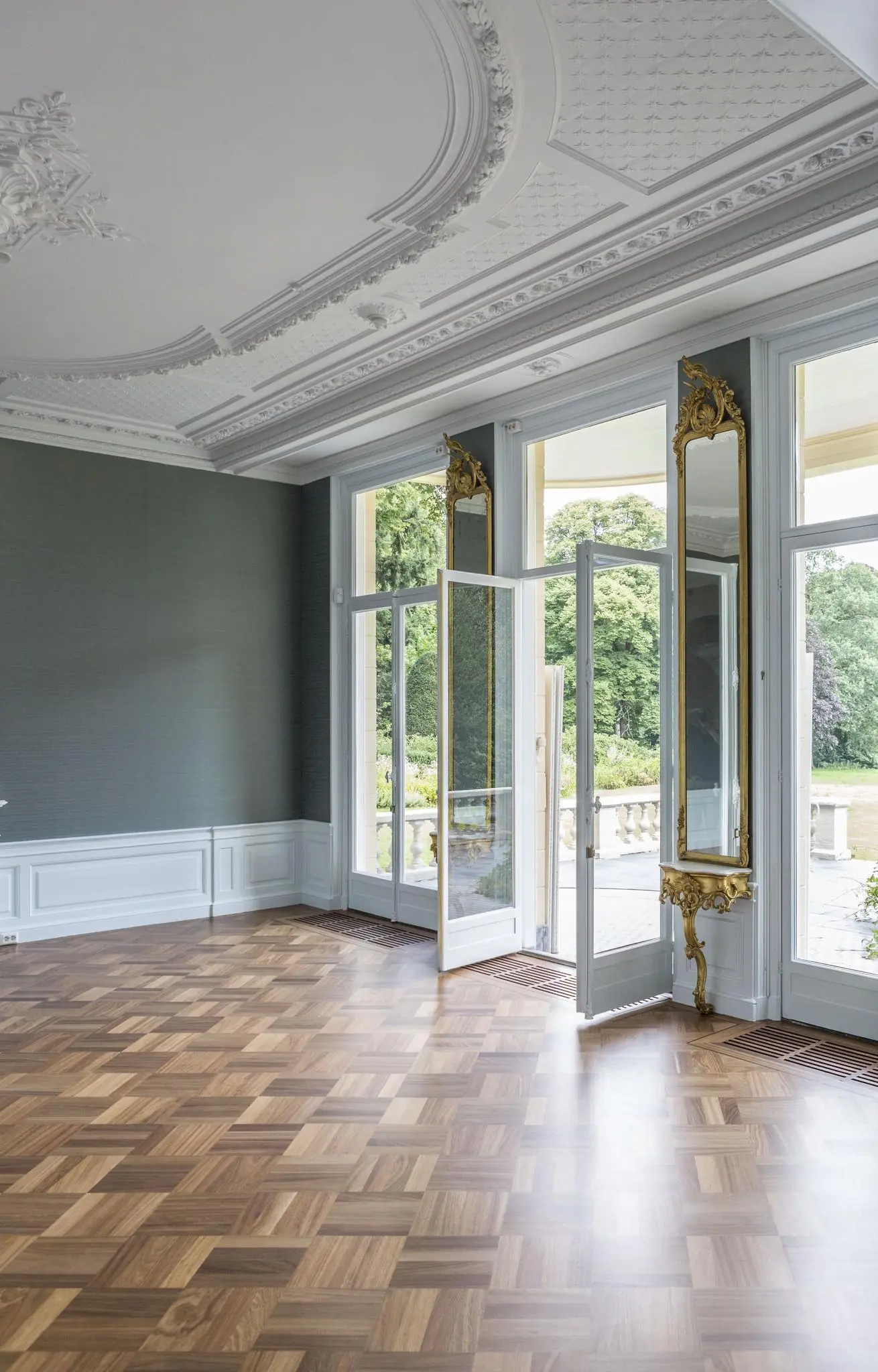 Luxe interieur van een klassieke kamer aan de Naarderstraat met visgraatparket, ornamentenplafond en openslaande deuren naar een tuin.