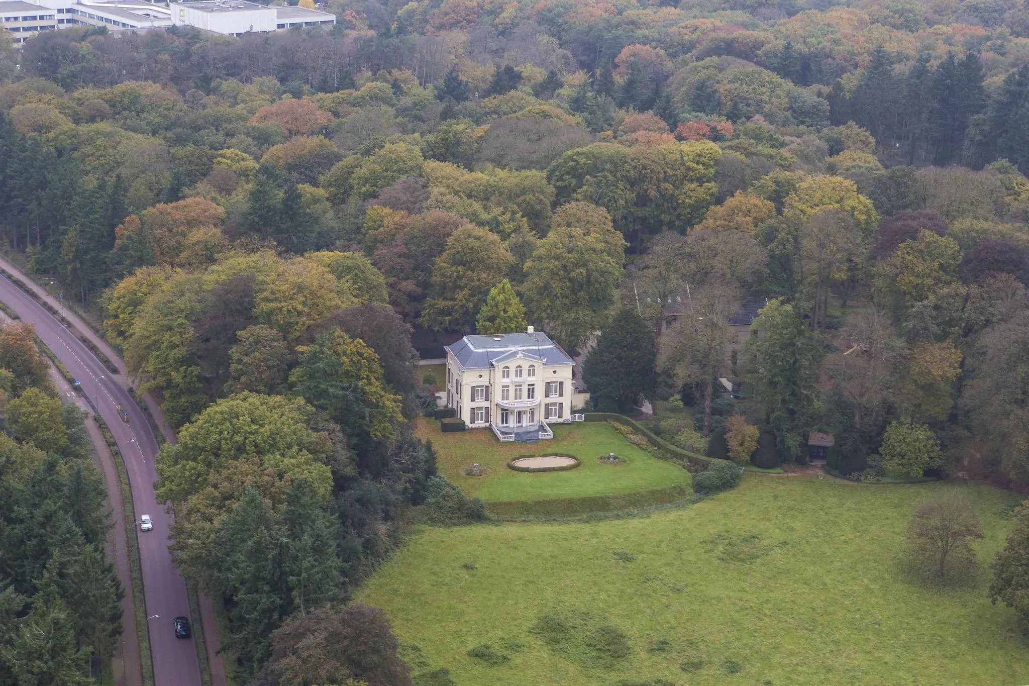 Luchtfoto van een grote, witte villa aan de Naarderstraat omringd door bosrijk gebied en een ruime tuin.