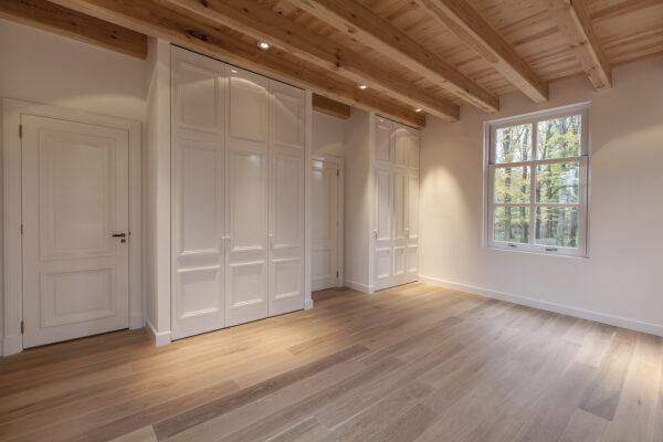 Lichte, lege kamer aan de Naarderstraat met houten vloer, ingebouwde kasten, houten balkenplafond en een raam met uitzicht op bomen.