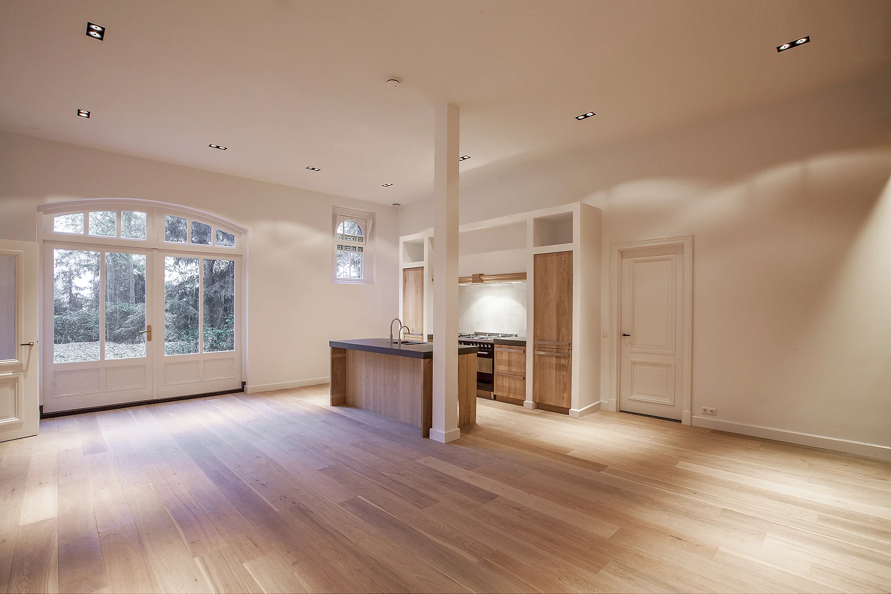 Lichte en ruime open woonkamer met houten vloer, moderne open keuken en grote ramen aan de Naarderstraat.