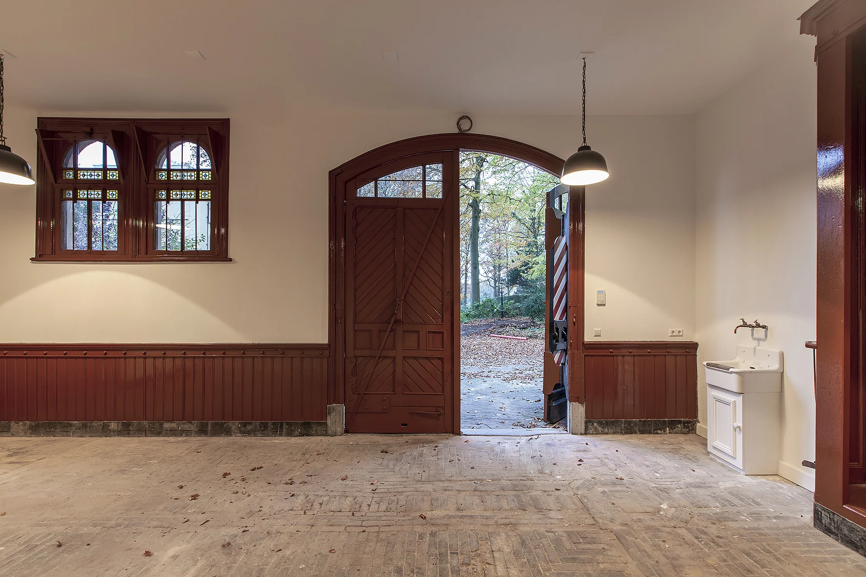 Interieur van een lege garage of bijgebouw aan de Naarderstraat met open houten deuren naar een bosrijke tuin.