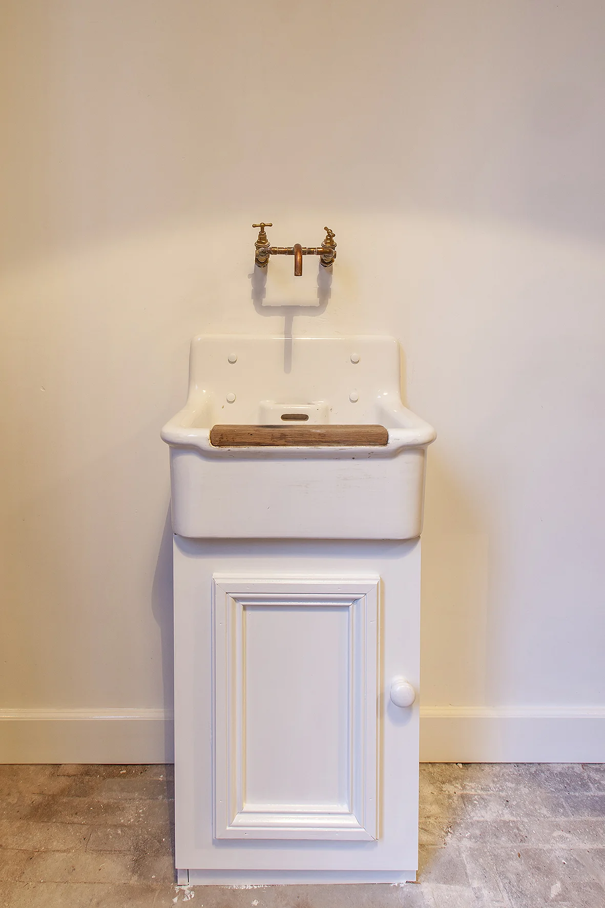 Wit, klassiek wastafeltje met messing kranen en houten leuning in een ruimte aan de Naarderstraat.