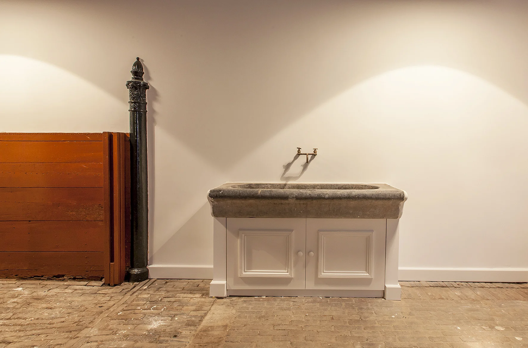 Rustieke wastafel met natuurstenen wasbak en messing kranen tegen een lichtgekleurde muur in een gerenoveerd interieur aan de Naarderstraat.