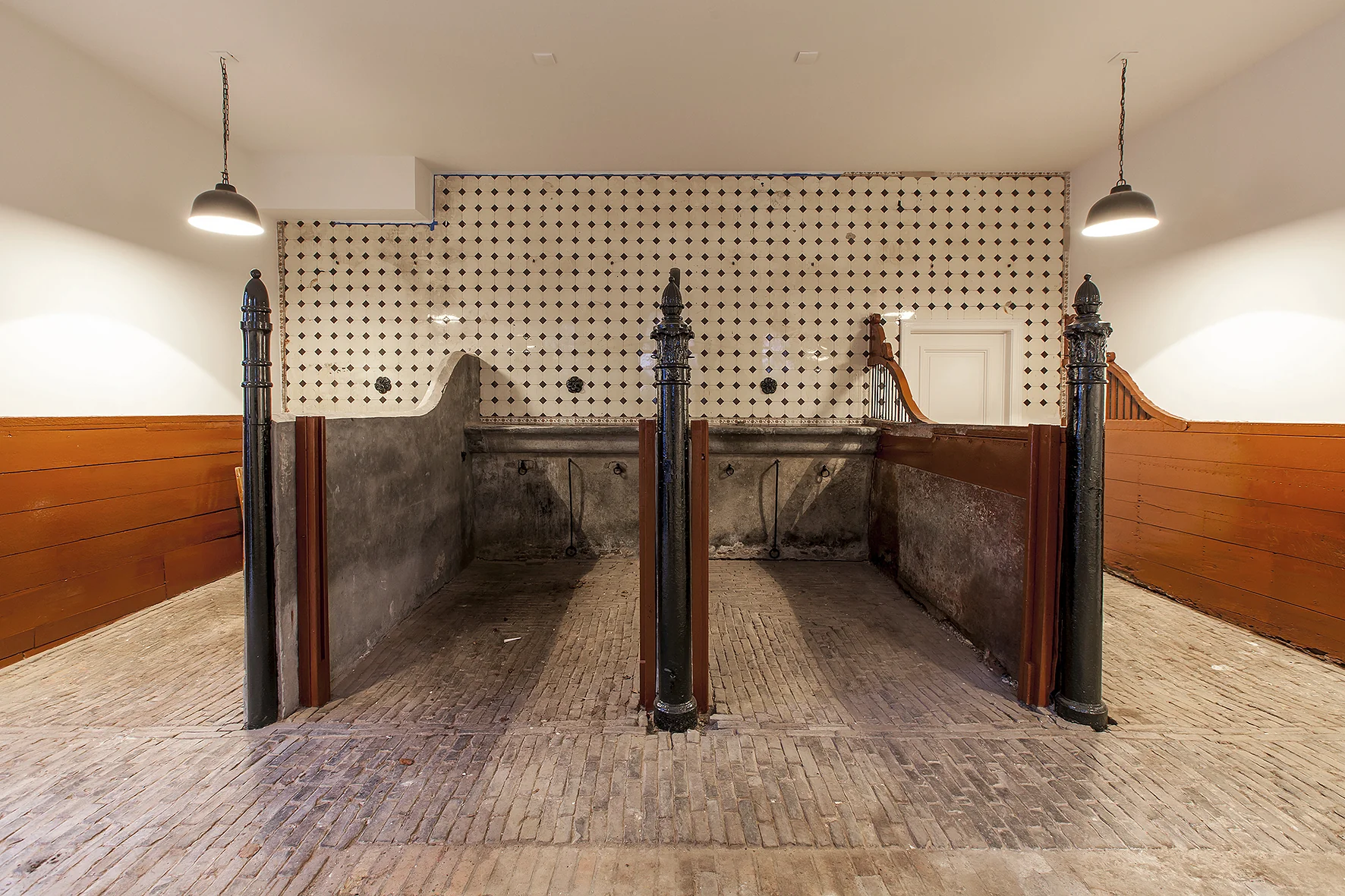Historische paardenstal in een gerenoveerd interieur aan de Naarderstraat met betegelde achterwand en houten scheidingswanden.