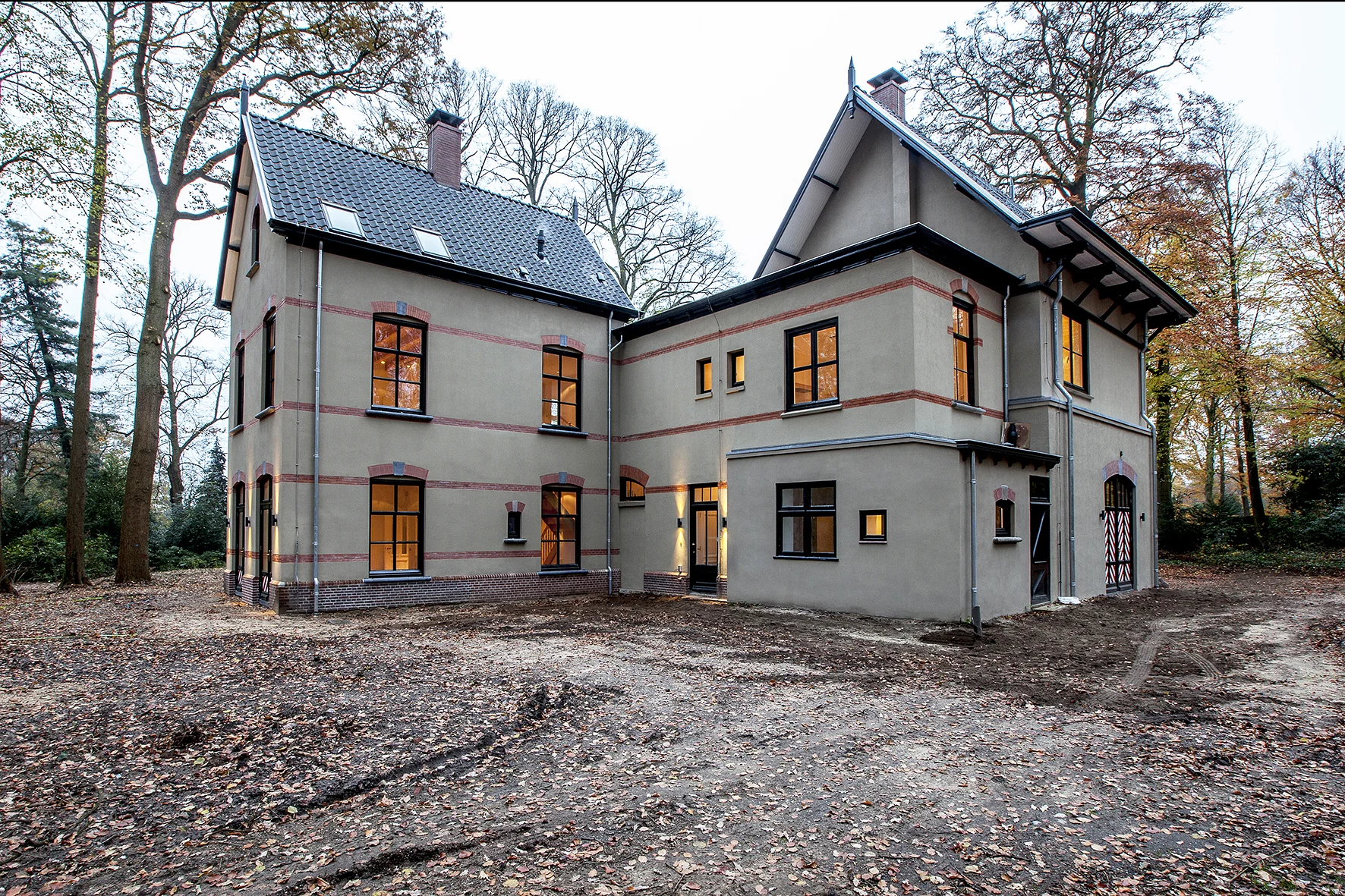 Gerenoveerde villa aan de Naarderstraat, omringd door bomen en herfstbladeren, met warme verlichting binnen.