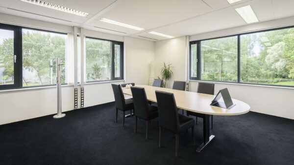 Vergaderruimte met ovale tafel, zes stoelen en grote ramen met uitzicht op groen bij Cypresbaan.