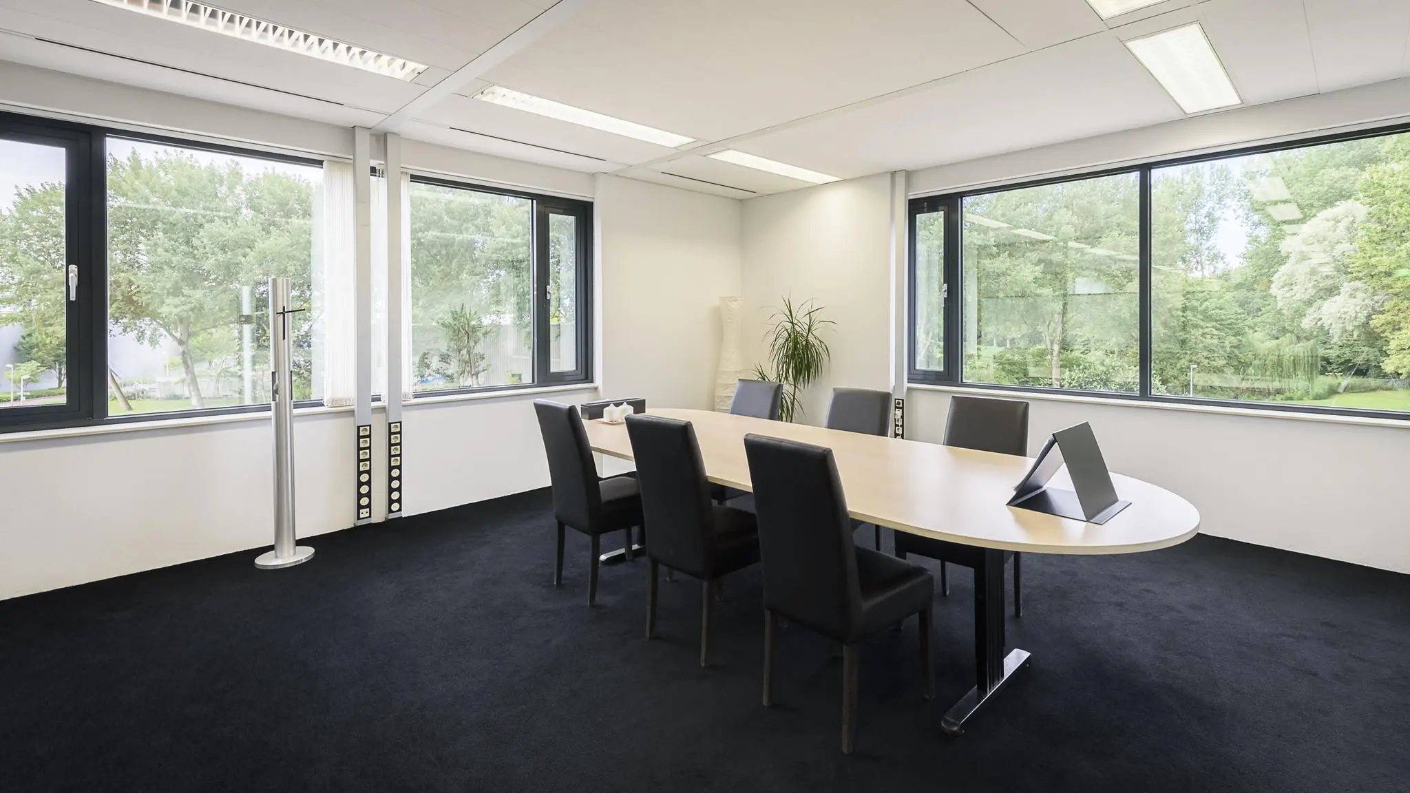 Vergaderruimte met ovale tafel, zes stoelen en grote ramen met uitzicht op groen bij Cypresbaan.