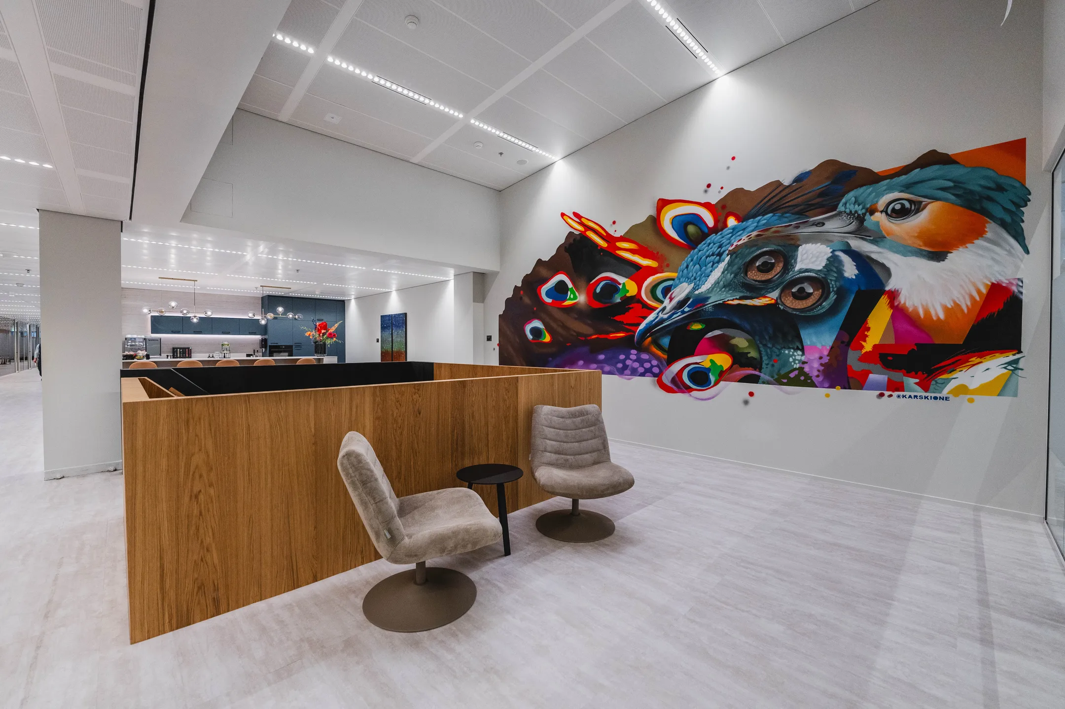 Een moderne kantoorruimte met stoelen en een kleurrijke muurschildering van een vogel.