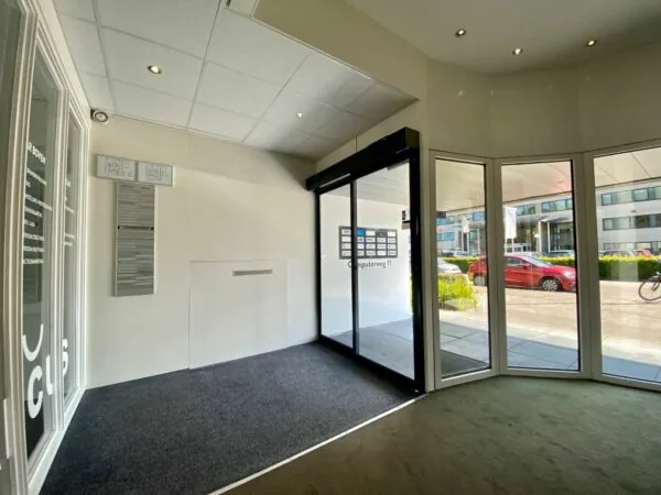 Ingang van een kantoorgebouw aan de Computerweg 11 met glazen draaideur en zicht op geparkeerde auto's buiten.