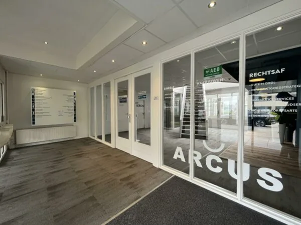 Ingang van bedrijfsverzamelgebouw Arcus aan de Computerweg, met glazen deuren en bewegwijzering naar verschillende bedrijven.