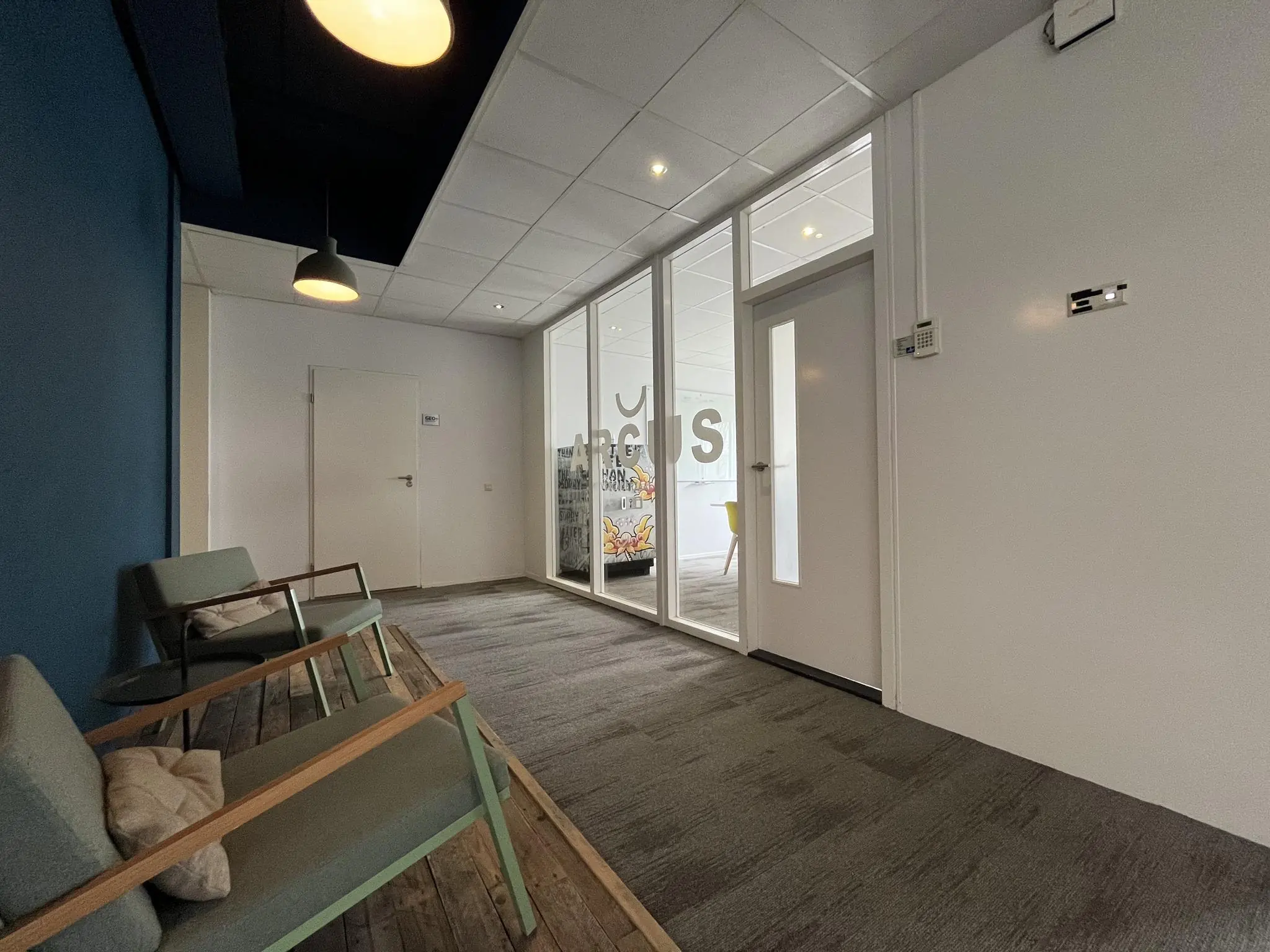 Moderne wachtruimte met stoelen en zicht op een kantoorruimte met de naam "ARCUS" op de glazen wand.
