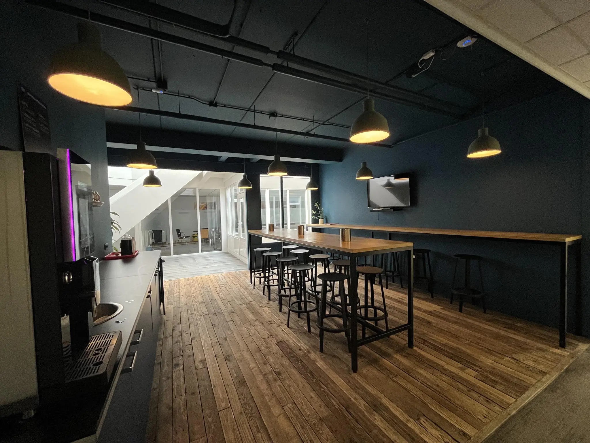 Moderne bedrijfskeuken aan de Computerweg met houten vloer, hoge tafels, barkrukken en warme hangverlichting.