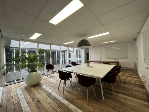 Vergaderruimte aan de Computerweg met houten vloer, grote plant, witte tafel en paarse stoelen.