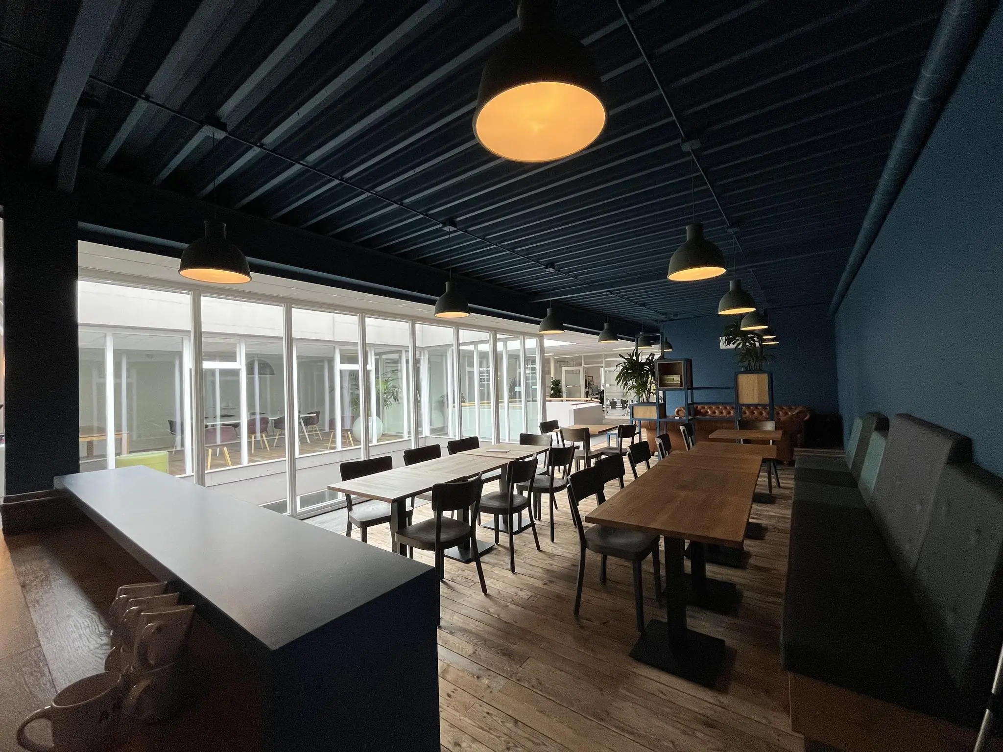 Moderne, sfeervol ingerichte kantineruimte aan de Computerweg met houten vloeren, lange tafels en veel natuurlijk licht via grote ramen.