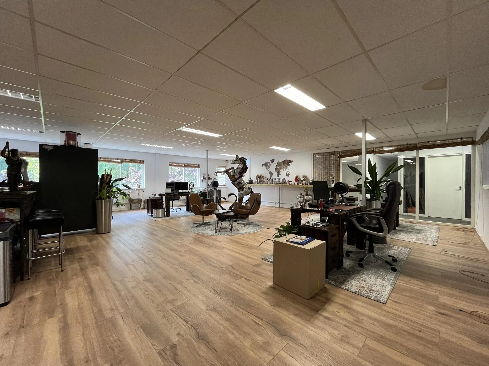 Ruim en modern kantoor aan de Computerweg met houten vloer, bureaus, kunstobjecten en grote ramen.