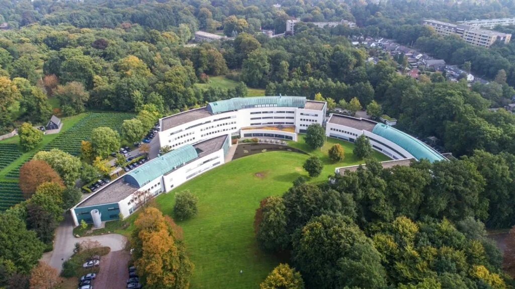 Luchtfoto van het gebogen gebouw van Ziekenhuis Reade locatie Sparrenheuvel, omringd door bosrijk gebied.