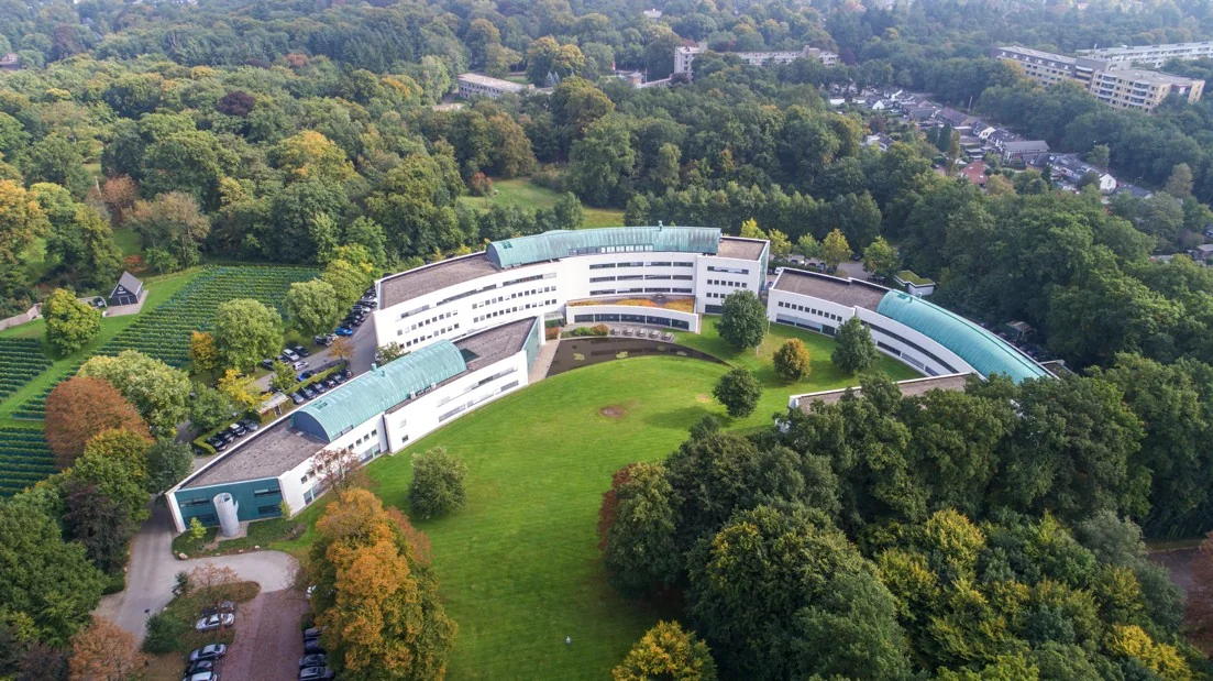 Luchtfoto van het gebogen gebouw van Ziekenhuis Reade locatie Sparrenheuvel, omringd door bosrijk gebied.