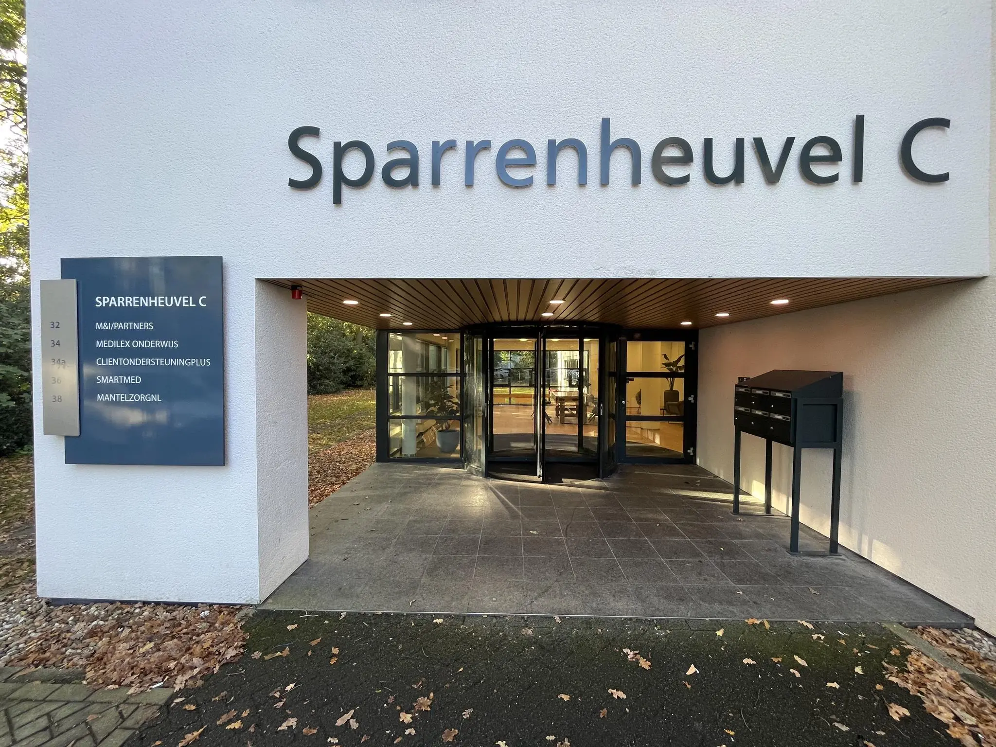 Ingang van kantoorgebouw Sparrenheuvel C met naambord en draaideur.