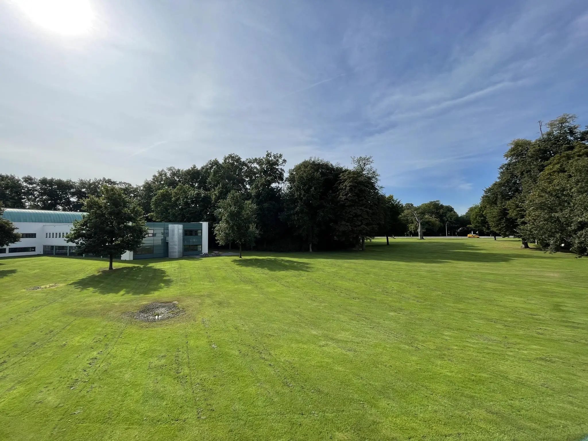 Groen grasveld met op de achtergrond het moderne gebouw Sparrenheuvel, omgeven door bomen onder een blauwe lucht.