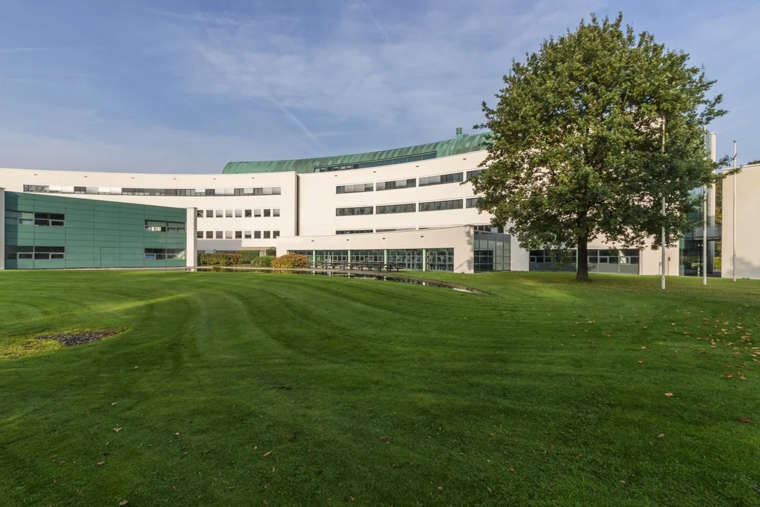 Modern gebouw van zorginstelling De Sparrenheuvel met een groen gazon en grote boom op de voorgrond.